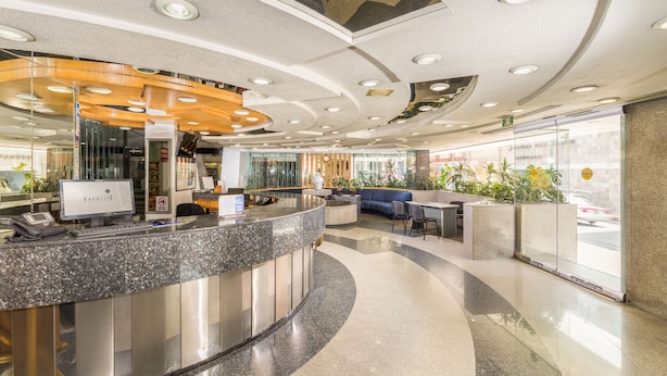 A modern reception area with a curved counter, a computer, and a seating area with a blue sofa. - Hotel Estoril (Mexico City)