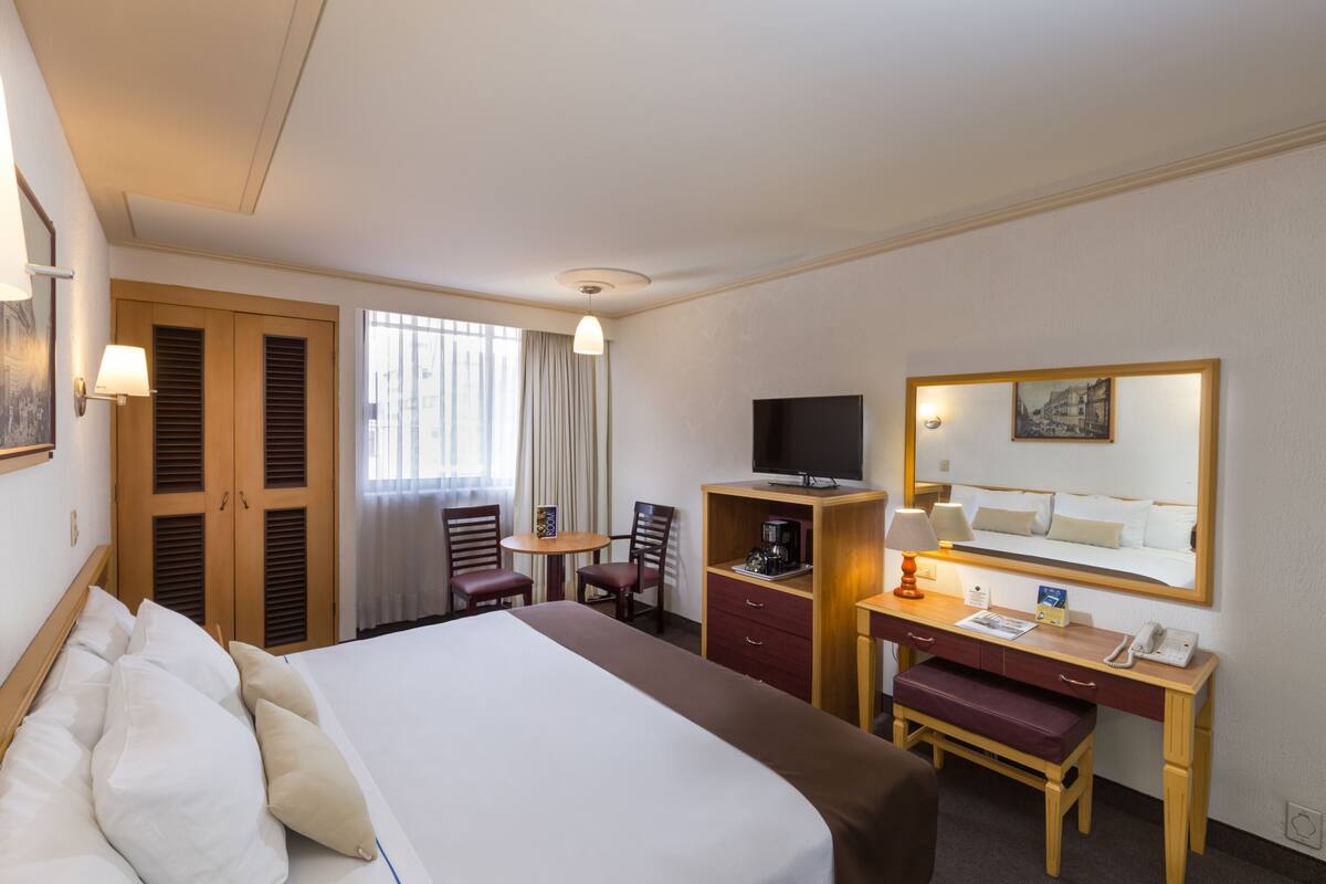 Habitación de hotel con una cama grande, un escritorio con teléfono, televisión y una pequeña mesa con sillas.