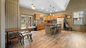 A spacious kitchen with wooden cabinets, a central island with stools, and pendant lighting. - Firefly @ Frio River Vacation Rentals (Concan)