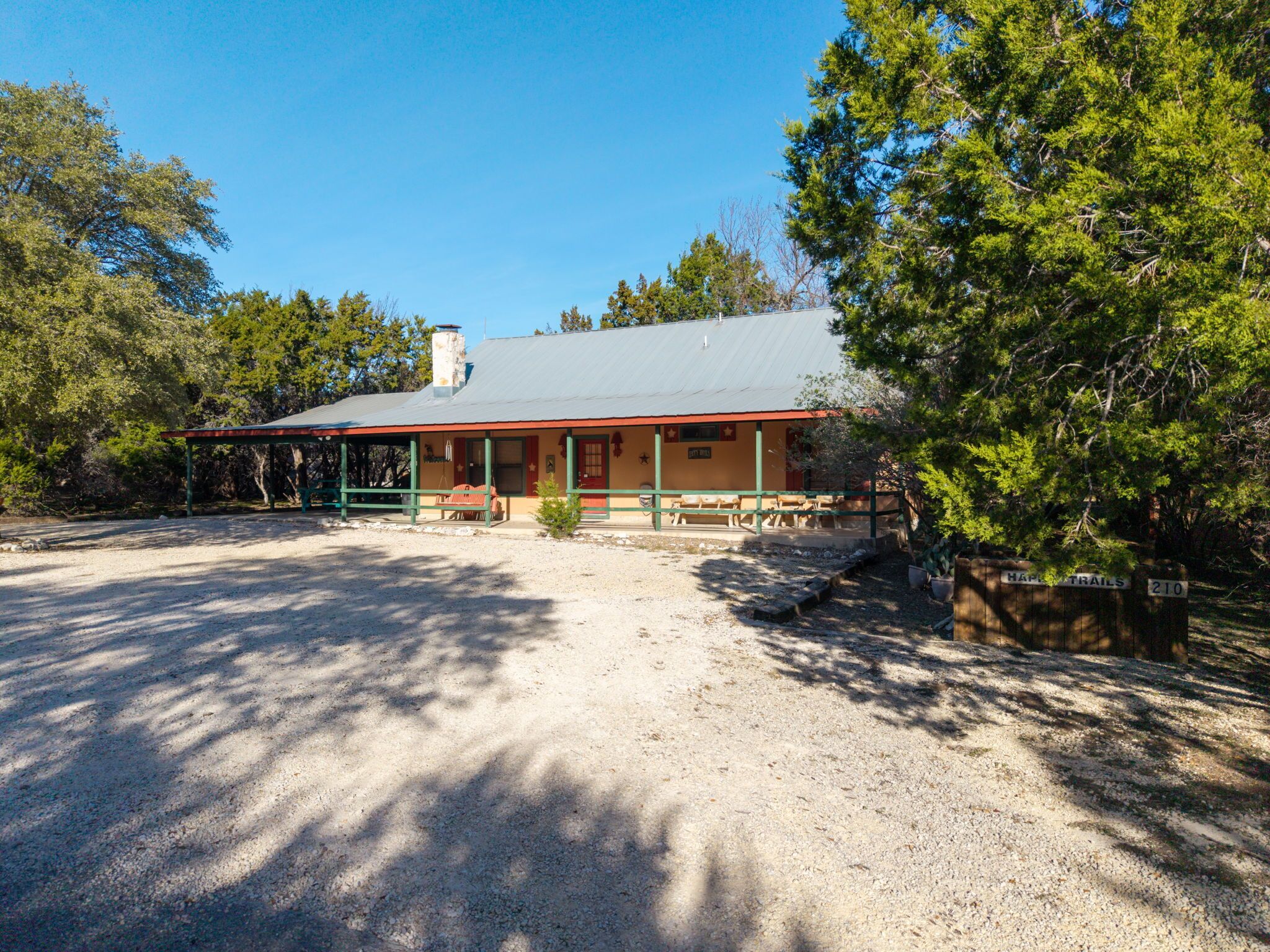 A rustic building with a covered porch, a chimney, and a gravel driveway.