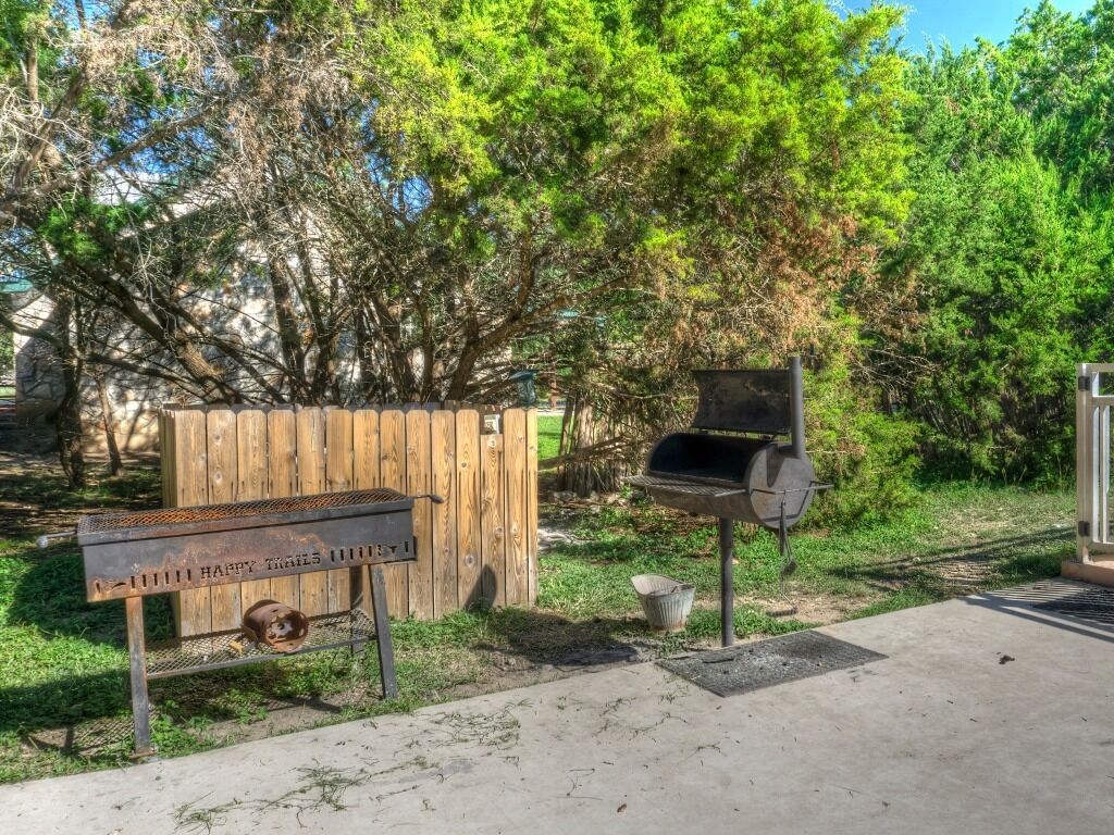 Un jardin avec une clôture en bois, un barbecue en métal et un banc agrémenté d’une pancarte.
