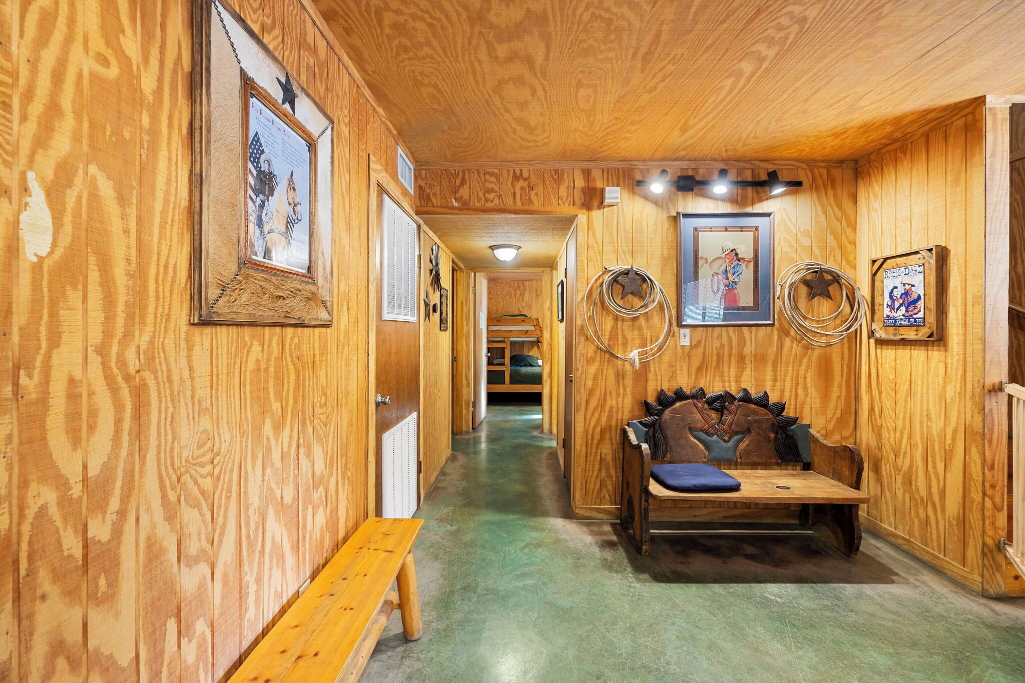 Een houten gang met ingelijste foto’s, een bankje en een bed in de verte.