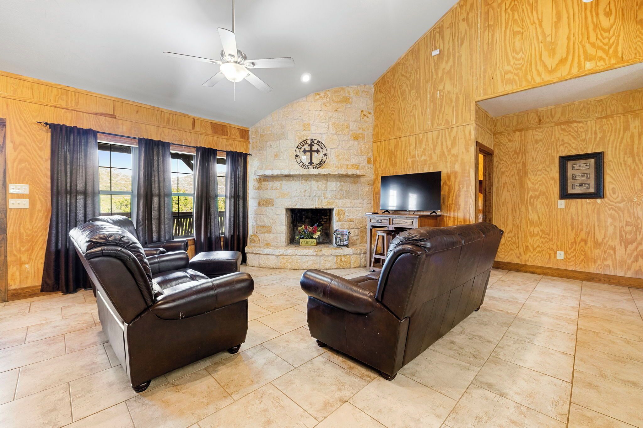 A living room with leather sofas, a stone fireplace, and a television.