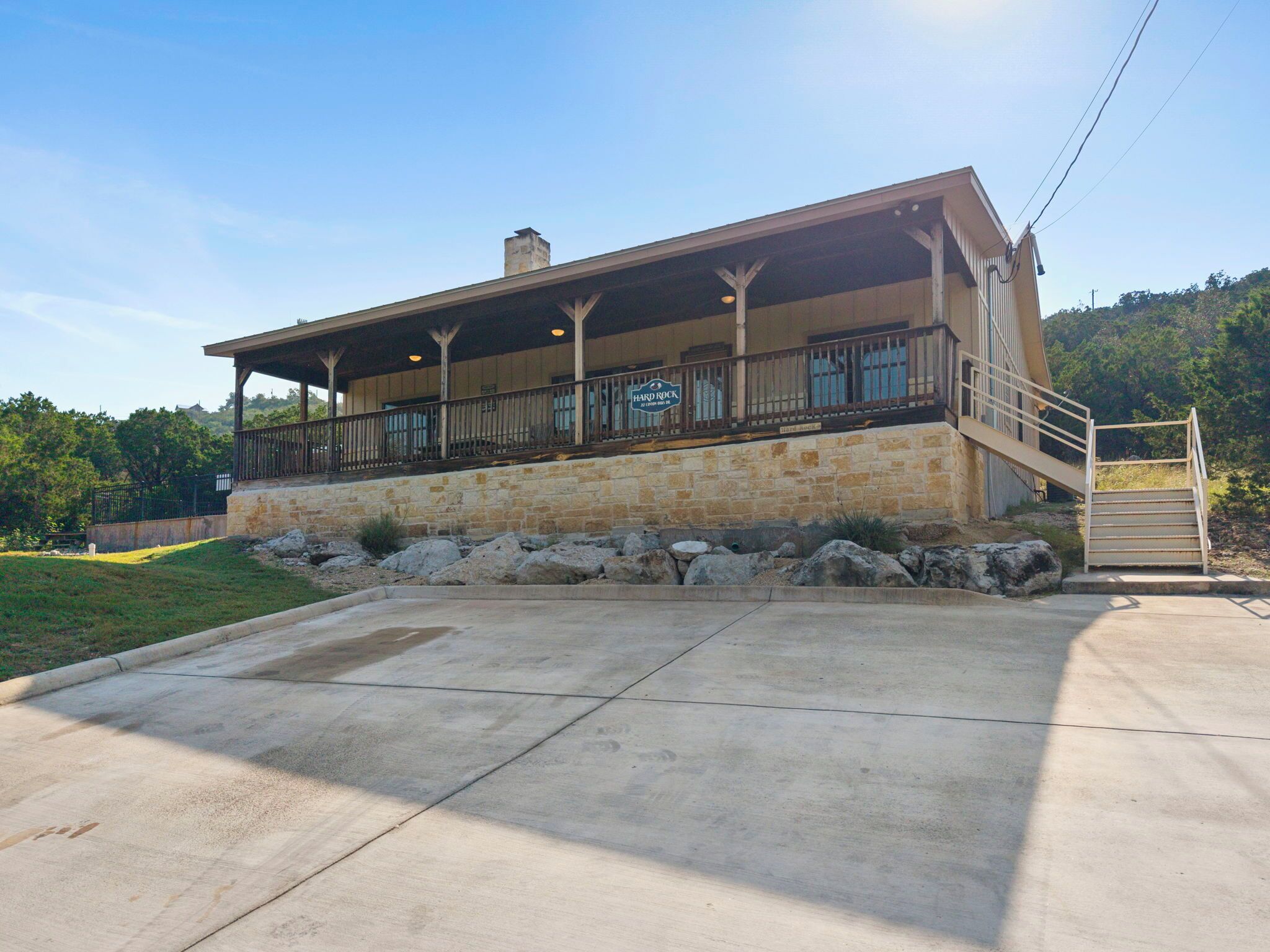 A building with a covered patio, stone foundation, and a staircase leading to an upper level.