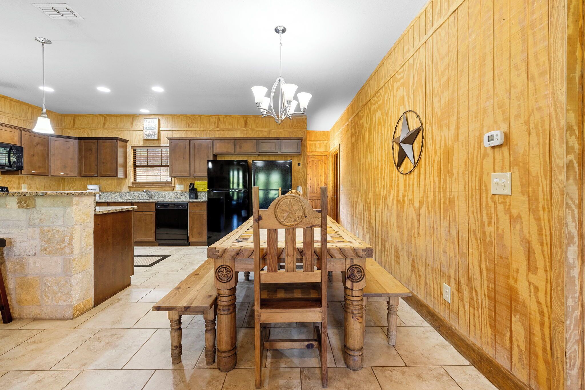 A kitchen with wooden cabinets, a central island, a dining table with a star-shaped headrest, and a chandelier.