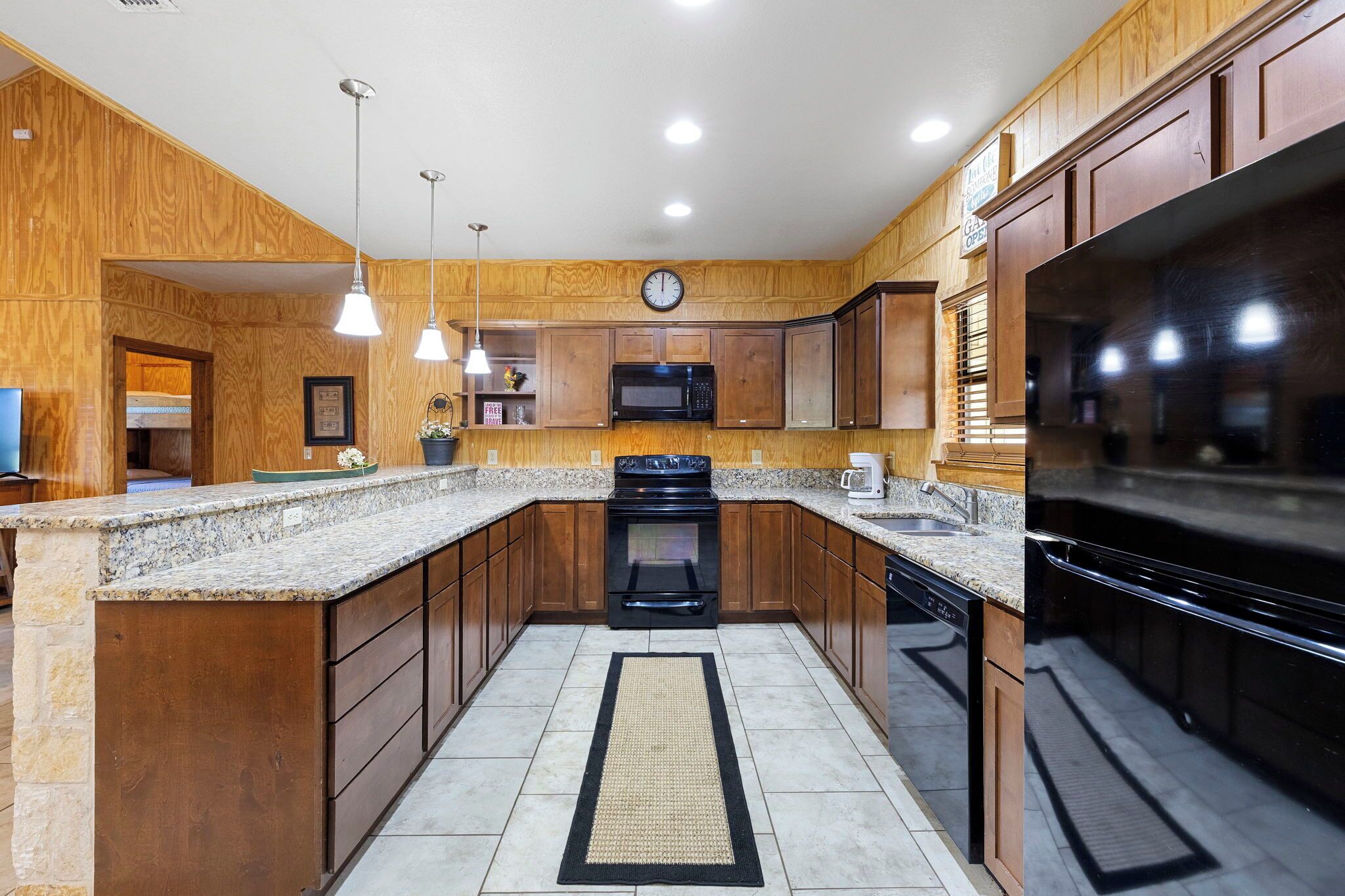 A kitchen with wooden cabinets, granite countertops, a black stove, a microwave, and a clock on the wall.