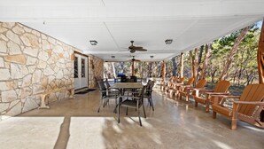 A covered patio with a stone wall, a dining table with chairs, and wooden Adirondack chairs. - Paloma Linda @ Frio River Vacation Rentals (Concan)