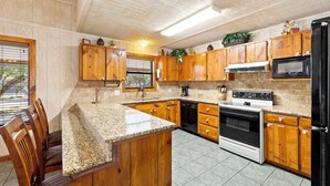 A kitchen with wooden cabinets, a granite countertop, a stove, an oven, a microwave, and a dishwasher. - Paloma Linda @ Frio River Vacation Rentals (Concan)