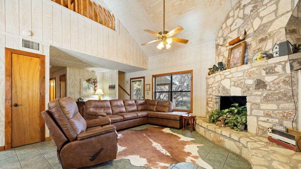 A spacious living room with a large sectional sofa, a stone fireplace, and a ceiling fan. - Paloma Linda @ Frio River Vacation Rentals (Concan)