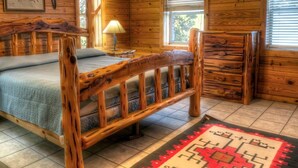 Ein Schlafzimmer in einer Holzhütte mit einem Bett, einem Nachttisch, einer Kommode und einem Fenster mit Jalousien.