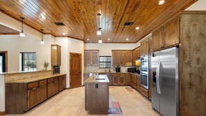 Una cocina amplia con armarios de madera, una isla central, electrodomésticos de acero inoxidable y techo de madera.