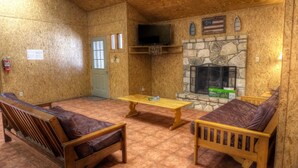 A cozy cabin interior with a stone fireplace, wooden furniture, and a television mounted above it. - Not To Worry, Wi-Fi, @ Frio River Vacation Rentals (Concan)
