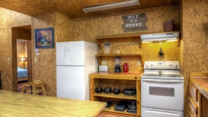A compact kitchen with a refrigerator, stove, and shelves with pots. A 'Not to worry' sign is visible on the wall. - Not To Worry, Wi-Fi, @ Frio River Vacation Rentals (Concan)