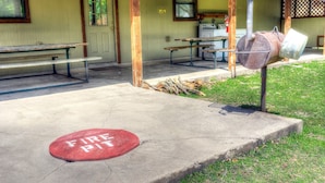 A fire pit area with a fire hydrant nearby, benches, and a building with a green door in the background. - Not To Worry, Wi-Fi, @ Frio River Vacation Rentals (Concan)