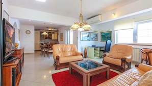 A spacious living room with leather sofas, a coffee table, and a television. There is a dining area with chairs and a table, and a kitchen in the background. - Apt w Jacuzzi, Balcony & sea View, 3 min to Beach (Dugi Rat)