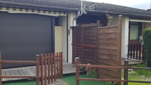 A residential property with a closed roller shutter garage door, a wooden fence, and a small porch area. - Duplex 24m2 Avec Terrasse et Chambre en Mezzanine. Proche du Mont Dore (La Bourboule)