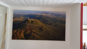 A room with a large landscape painting of a mountainous area and a rope bridge. - Duplex 24m2 Avec Terrasse et Chambre en Mezzanine. Proche du Mont Dore (La Bourboule)