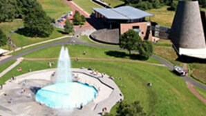 An aerial view of a park with a central fountain, a building with a flat roof, and a large chimney-like structure. - Duplex 24m2 Avec Terrasse et Chambre en Mezzanine. Proche du Mont Dore (La Bourboule)
