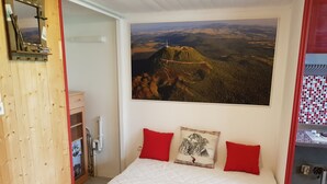 A bedroom with a large bed, a wooden wardrobe, a mirror, a painting of a landscape, and a small table with items on it. - Duplex 24m2 Avec Terrasse et Chambre en Mezzanine. Proche du Mont Dore (La Bourboule)