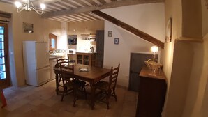 A rustic kitchen with wooden beams, a dining table with chairs, and a refrigerator. - Charming village house (year-round rental) (Montmeyan)