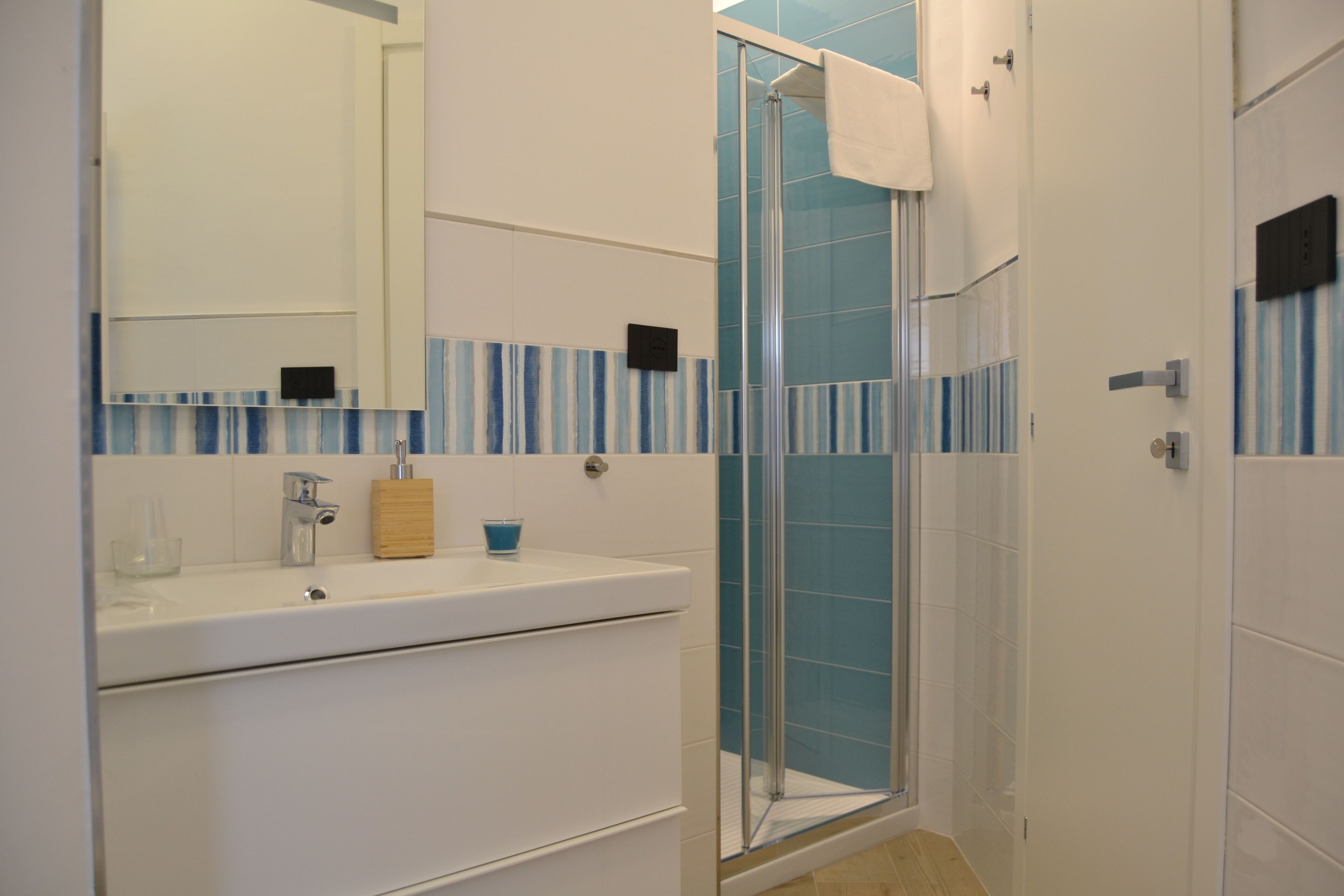 A modern bathroom with a glass shower enclosure, a white sink, and a mirror.
