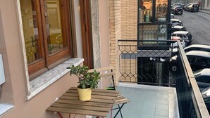 A balcony with a wooden table and chairs, a potted plant, and a view of parked cars and buildings. - Alleria Holiday Home (Salerno)