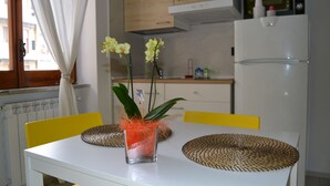 A kitchen with a white table, yellow chairs, a glass vase with flowers, and a microwave. - Alleria Holiday Home (Salerno)