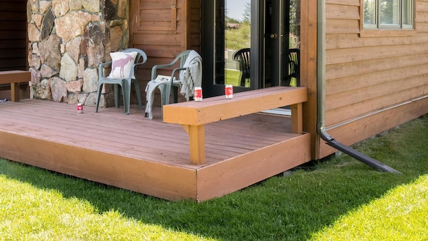A two-story wooden cabin with a stone chimney, a balcony, and a deck area with outdoor seating. - Outpost: Teton Shadows Eagle D - Close to Tetons! (Jackson)