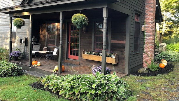 Ein Haus mit Veranda, Essbereich und Garten mit Pflanzen und Kürbissen.