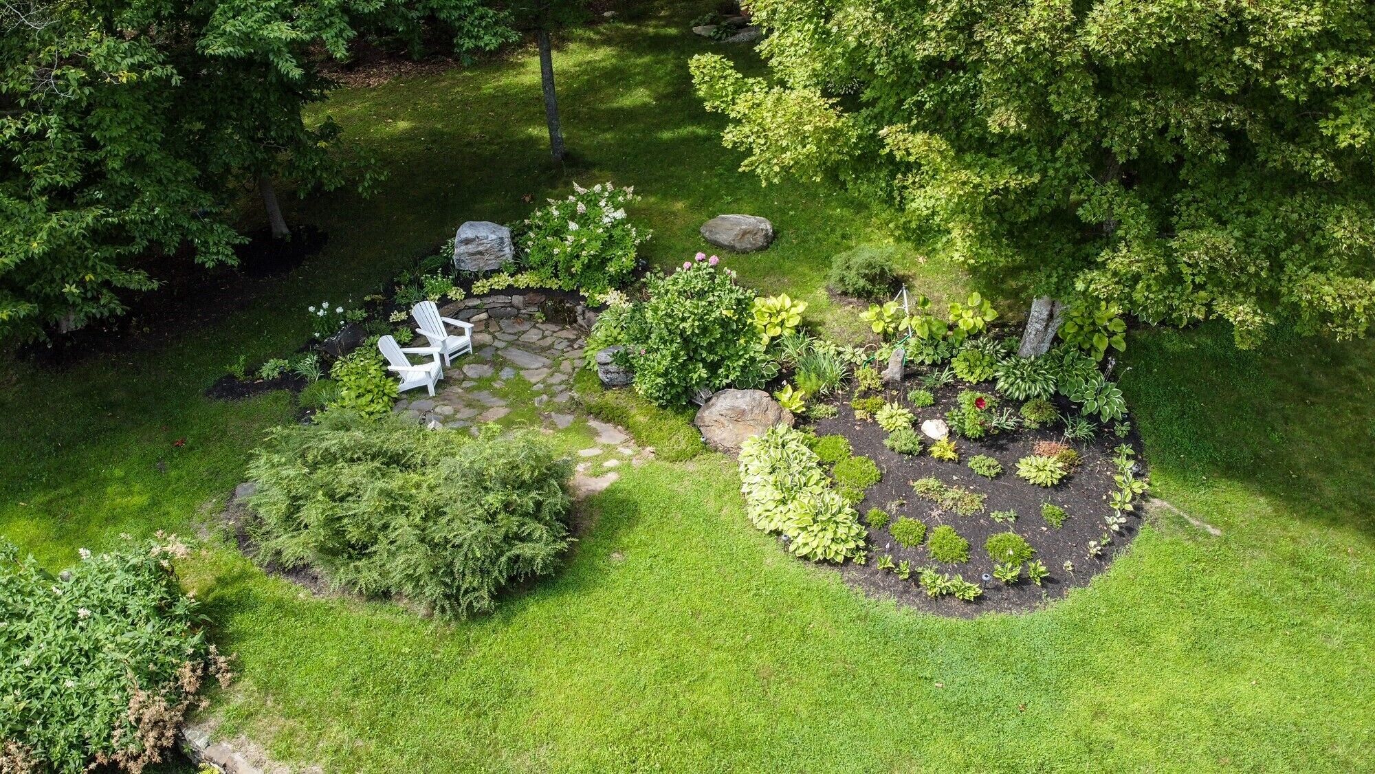 Um jardim bem cuidado com um caminho de pedra, área de estar e diversos arbustos.