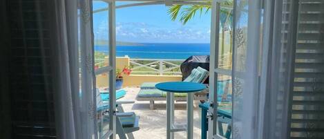 Un balcon avec une table et des chaises, une vue sur l’océan et une plante tropicale.