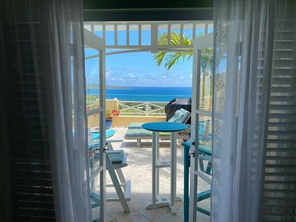 A balcony with a table and chairs, a view of the ocean, and a tropical plant.