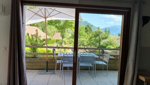 A balcony with a table and chairs, a view of greenery and mountains, and a sliding glass door. - Le Typique Atypique Spacieux 140 m2 au Centre du Hameau de Perroix (talloires montmin)