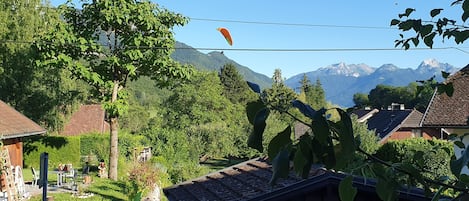 Paisagem rural com uma casa, uma placa indicando 'CHEMIN de PRE MONTEUX' e montanhas ao fundo.