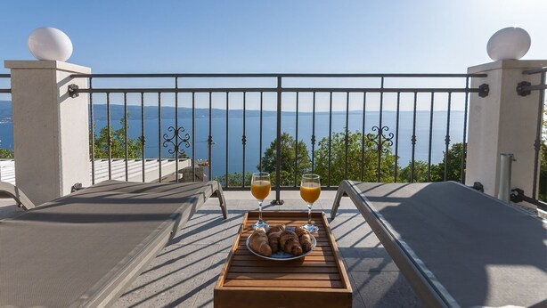 Un balcon avec une table dressée pour deux, un verre de jus d’orange et une assiette de croissants, le tout offrant une vue imprenable sur la mer.