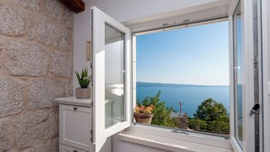 Une pièce avec un mur en pierre, une armoire blanche et une fenêtre donnant sur la mer.