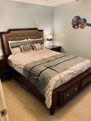 Una cama bien hecha con una manta a rayas y almohadas, una mesita de noche con una lámpara y un adorno en la pared.