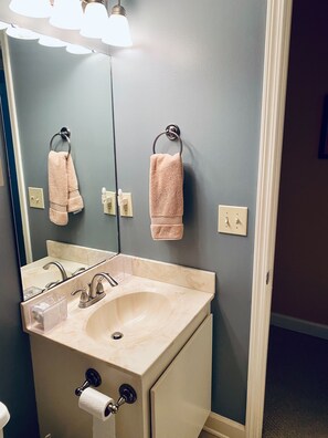 Un baño con un lavamanos color beige, dos toallas, un espejo y un dispensador de papel higiénico.