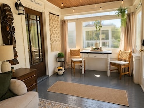 A cozy room with a wooden floor, a desk with chairs, a lamp, and a wall-mounted macrame piece.