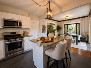 A modern kitchen with stainless steel appliances, a central island with bar stools, and a dining area with a view.