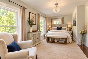 A bedroom with a large bed, a chair, a dresser, and a chandelier.