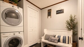 A laundry area with stacked washers and dryers, a bench with pillows, a rug, and a sign on the wall. - Comfy Updated Historic Gem Pets OK 3B Vibrant Area (Painesville)