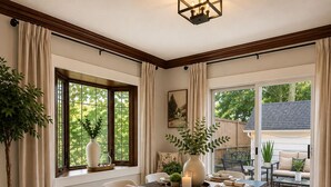 A dining area with a dark wooden table, white chairs, and a large window with curtains. - Comfy Updated Historic Gem Pets OK 3B Vibrant Area (Painesville)