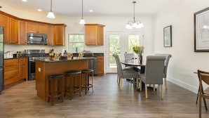 Una cocina moderna con armarios de madera, una isla central con taburetes y una zona de comedor con mesa y sillas.