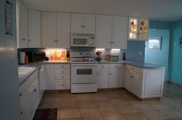 A kitchen with white cabinets, a microwave, a stove, and a sink.