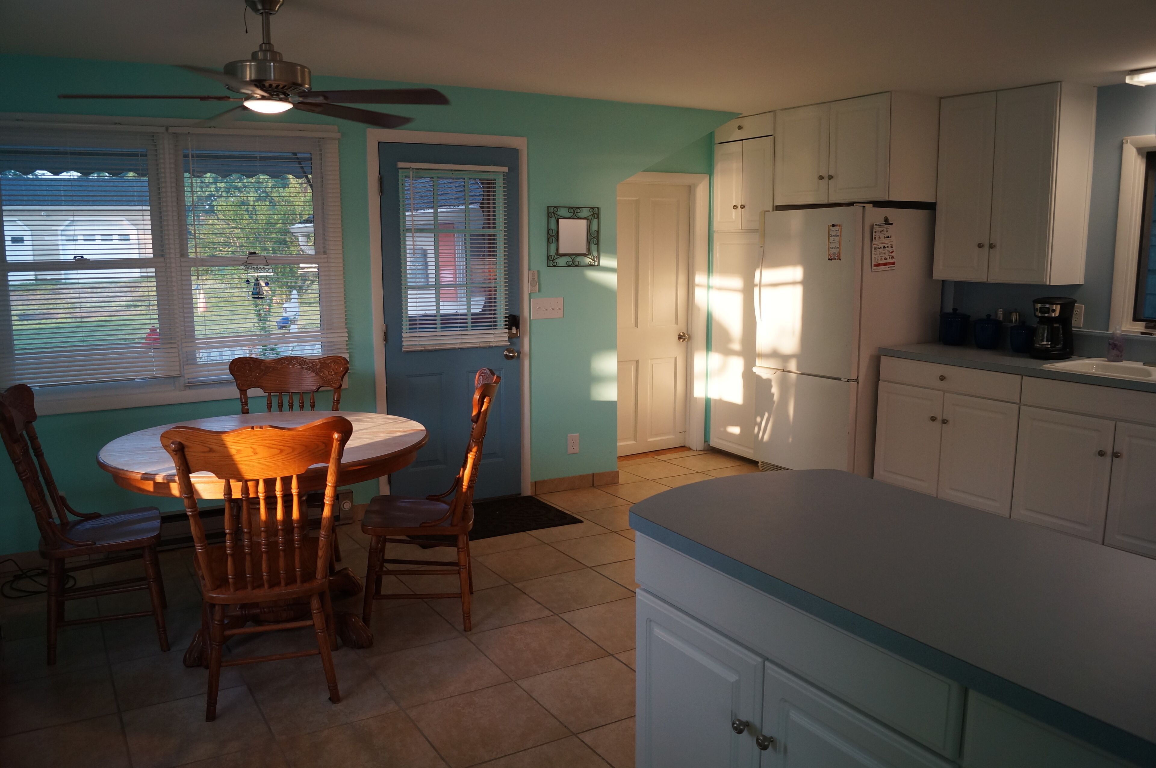 Une cuisine avec une table et des chaises, des armoires blanches et un ventilateur de plafond.