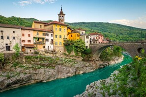 Eine historische Stadt mit einer Steinbrücke über einem türkisfarbenen Fluss, bunten Gebäuden und einer Erhebung im Hintergrund.