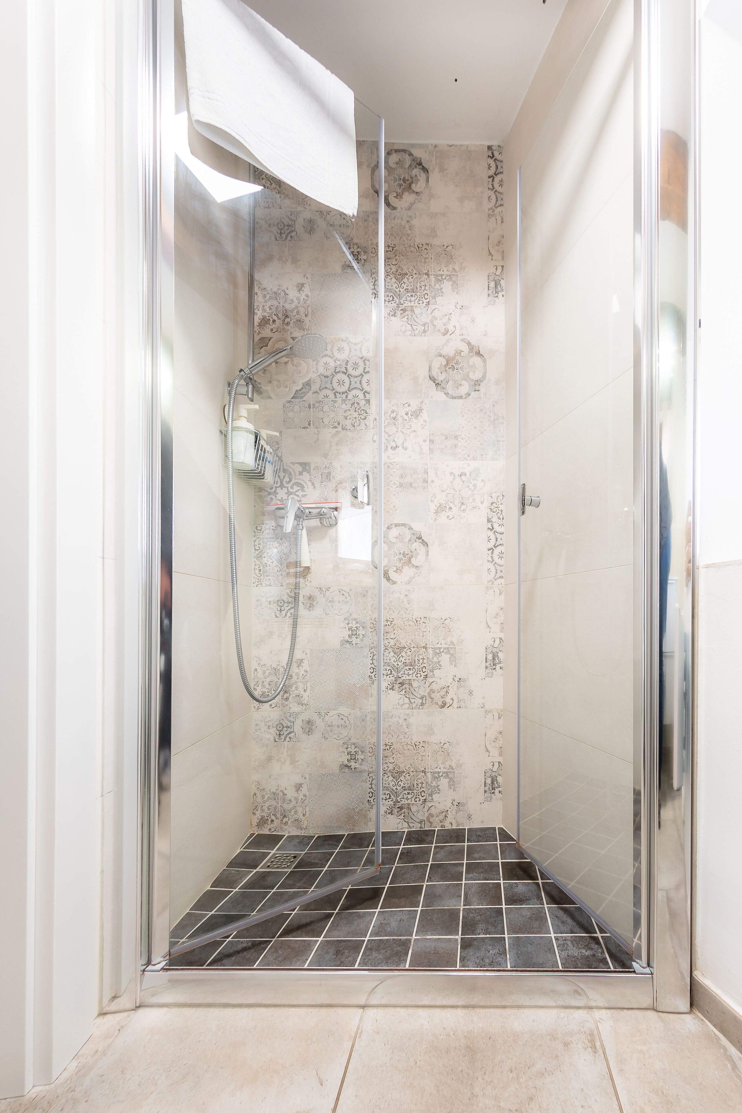 Una cabina doccia con pareti in vetro, pavimento piastrellato e piastrelle decorative.