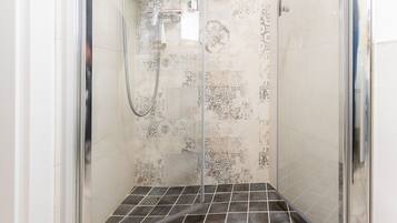 Una cabina doccia con pareti in vetro, pavimento piastrellato e piastrelle decorative.