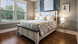 Un dormitorio con una cama grande, dos lámparas de noche, un banco al pie de la cama y una ventana con persianas.